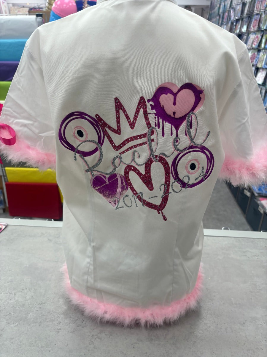 This listing offers a unique personalized glitter and diamante crown with a pink and glitter silver layered design, complete with your name and leavers dates. Feel like royalty on your special day with the stunning crown, eye, and heart designs. The pink feather accents on the sleeves and shirt lining add a touch of elegance, making this signing shirt a cherished memento for years to come. Show off your individuality with the added pink bows on the sleeves.